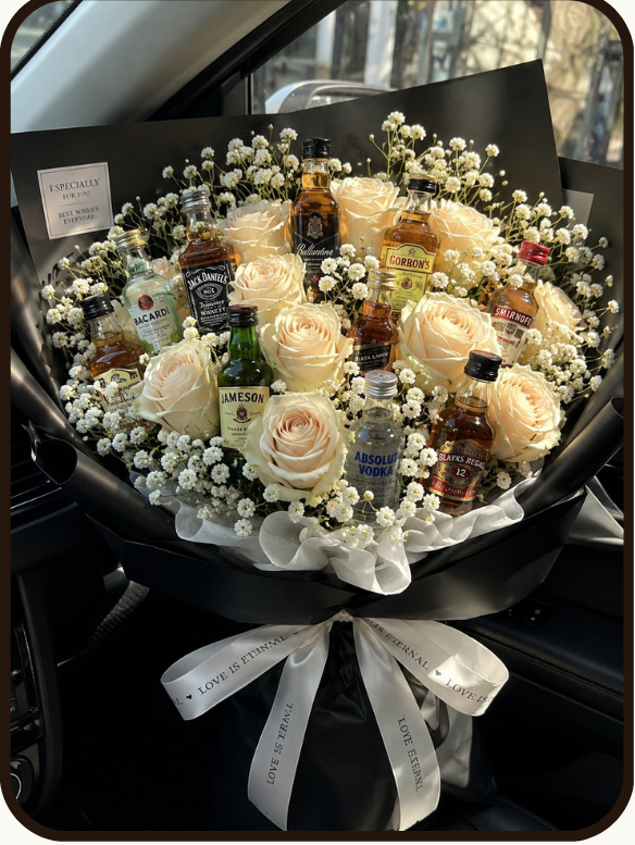 A product listing graphic for a 'Grand Celebration Mix' bouquet from DrapedNuts. The image features a photo of a black flower box containing a mix of white and black roses, chocolates, and biscuits, with a silver ribbon.